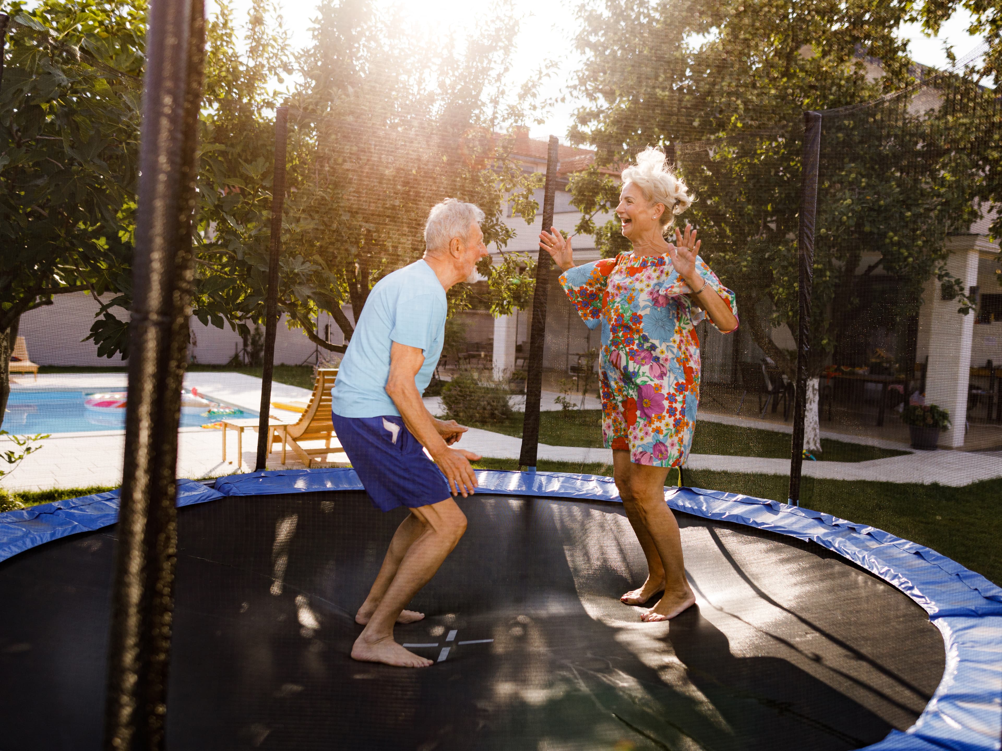 Active elderly couple jumping on a trampoline in a sunny backyard
